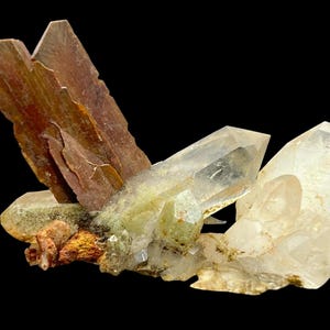 Puede incluir: Un grupo de cristales de cuarzo transparentes con un espécimen mineral marrón y estratificado. Los cristales de cuarzo son translúcidos y tienen un brillo vítreo. El espécimen mineral marrón es opaco y tiene una textura rugosa.
