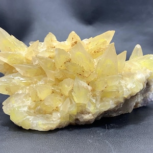 Könnte beinhalten: Ein Cluster aus gelben Calcitkristallen mit einer rauen, natürlichen Textur. Die Kristalle sind spitz und zugespitzt und bilden ein dramatisches Display.