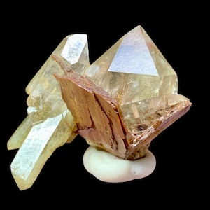 Puede incluir: Un grupo de cristales de cuarzo transparentes con una matriz mineral marrón y estratificada. Los cristales son translúcidos y tienen un ligero tono amarillo. La matriz es rugosa y texturizada.