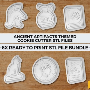 Op de afbeelding: Een verzameling van zes witte koekjessnijders in de vorm van oude artefacten, waaronder een helm, vaas, boek, kat, munt en tablet. De tekst "ANCIENT ARTIFACTS THEMED COOKIE CUTTER STL FILES -6X READY TO PRINT STL FILE BUNDLE-" is zichtbaar.