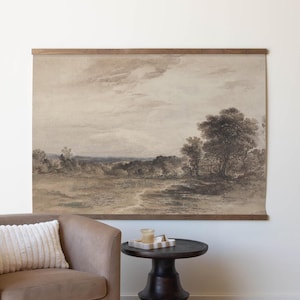 May include: A brown armchair with a white throw pillow sits in front of a framed landscape print of a field with trees. A small wooden side table with a round top sits next to the chair.