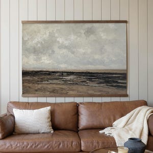 May include: A brown leather sofa with a striped pillow and a cream-colored throw blanket. A round wooden coffee table holds a candle, a decorative tray, and a dark blue vase. A landscape painting hangs above the sofa.