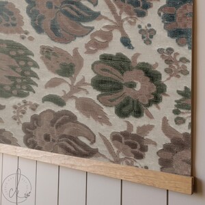 May include: Floral fabric wall hanging with a light beige background and large, detailed flowers in shades of brown, green, and blue. The fabric is mounted on a natural wood frame, creating a decorative piece for home decor.