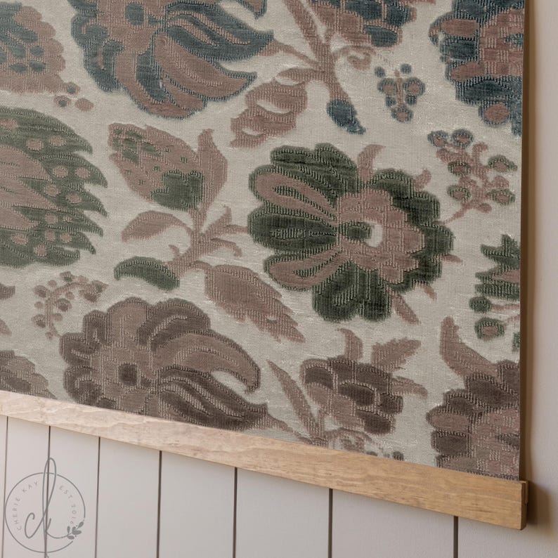 May include: Floral fabric wall hanging with a light beige background and large, detailed flowers in shades of brown, green, and blue. The fabric is mounted on a natural wood frame, creating a decorative piece for home decor.