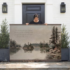 May include: A large framed landscape art print featuring a serene lake scene with trees and islands. The artwork has a vintage aesthetic with soft colors and a wooden frame. Text is visible on the artwork. The overall theme is nature and home decor.