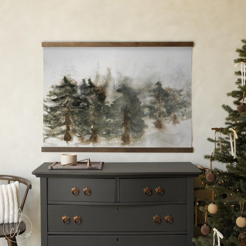 May include: A watercolor print of a forest scene, featuring evergreen trees in shades of green and brown, mounted on a wooden frame. The artwork hangs above a dark gray dresser with ornate bronze knobs. A Christmas tree with ornaments is in the background.