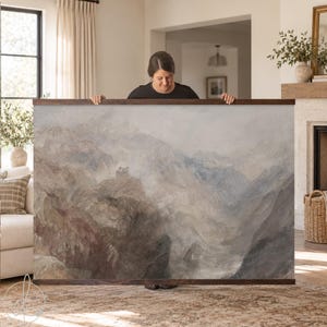 A large rectangular landscape wall art print featuring a muted watercolor painting of rugged mountain peaks in shades of gray, brown, and soft blue, secured between two horizontal dark wood hanging rails at the top and bottom.