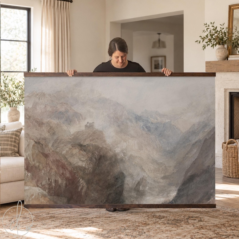 A large rectangular landscape wall art print featuring a muted watercolor painting of rugged mountain peaks in shades of gray, brown, and soft blue, secured between two horizontal dark wood hanging rails at the top and bottom.