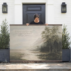 May include: A large landscape art print with a wooden frame. The artwork depicts a serene river scene with trees and mountains in muted tones. The text "You keep him in perfect peace whose mind is stayed on you, because he trusts in you. Isaiah 26:3" is visible.