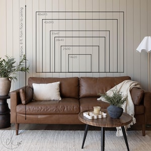 May include: A brown leather sofa with a striped pillow and a cream-colored throw blanket. A wooden coffee table with a decorative tray and a black vase with greenery. The wall displays framed rectangles with dimensions from 14x20 inches to 48x69.5 inches.