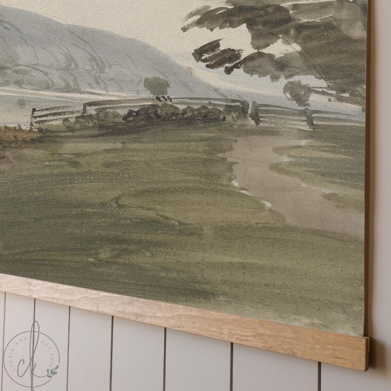 May include: Watercolor landscape art print featuring a serene countryside scene. The artwork depicts rolling hills, a winding path, and a fence, all rendered in muted green, gray, and brown tones. The print is mounted on a wooden frame.