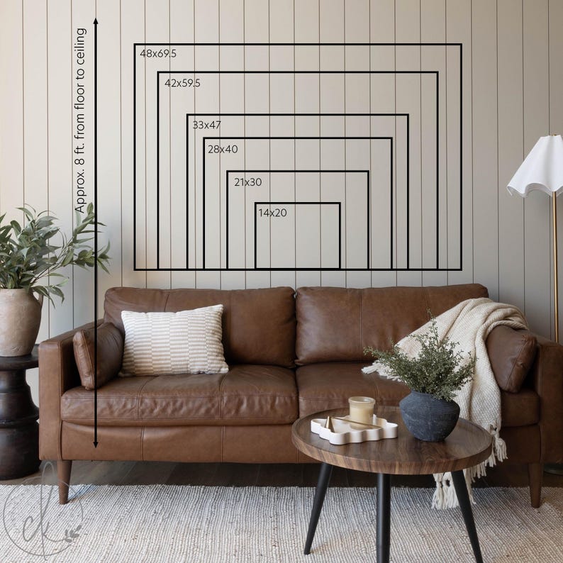 May include: A brown leather sofa with a striped cushion and a cream throw. A wooden coffee table with a decorative tray and a black vase with greenery. The wall displays framed rectangles with dimensions from 35.6x50.8cm to 121.9x176.5cm.