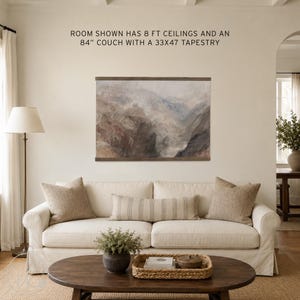 May include: A landscape tapestry featuring a muted mountain scene with brown and grey tones, framed by dark wood rails. The text above reads: ROOM SHOWN HAS 8 FT CEILINGS AND AN 84" COUCH WITH A 33X47 TAPESTRY. The tapestry is displayed on a plain wall.