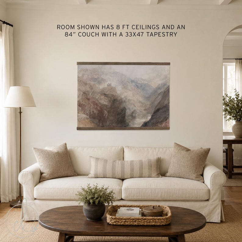 May include: A landscape tapestry featuring a muted mountain scene with brown and grey tones, framed by dark wood rails. The text above reads: ROOM SHOWN HAS 8 FT CEILINGS AND AN 84" COUCH WITH A 33X47 TAPESTRY. The tapestry is displayed on a plain wall.