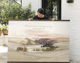 May include: A large rectangular wall hanging featuring a watercolor landscape of rolling hills and a valley under a soft pink sky. The text reads: His mercies are new every morning. LAMENTATIONS 3:22. It has dark wooden rails at the top and bottom.