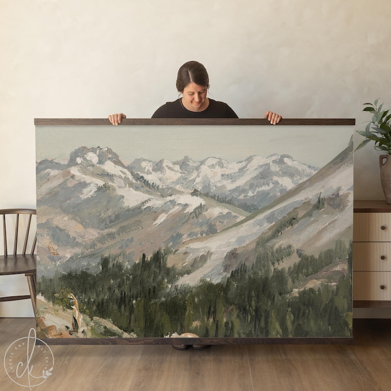 May include: Large landscape painting depicting a mountain range with snow-covered peaks and a forest in the foreground. The artwork is framed in dark wood. The colour palette includes shades of green, grey, and white.