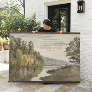 May include: A large, rectangular wall art piece with a watercolor landscape scene featuring a lake, trees, and a path. The artwork has a dark brown frame and includes the text "THE LORD IS MY SHEPHERD...HE RESTORES MY SOUL. PSALM 23:1-3."