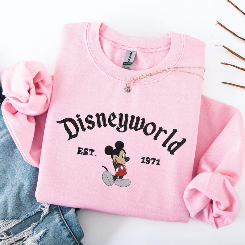 A pink sweatshirt with the text "Disneyworld" and a Mickey Mouse graphic, along with the text "EST. 1971" printed on it.