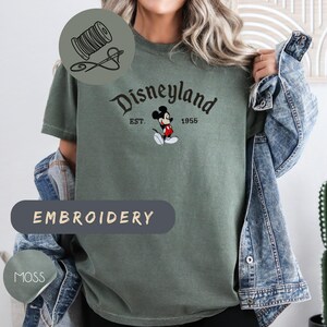 A person wearing a green t-shirt with the text "Disneyland EST. 1956" and a Mickey Mouse graphic, along with a denim jacket.