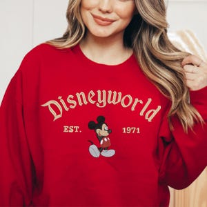 A woman wearing a red sweater with the text "Disneyworld EST. 1971" and a Mickey Mouse graphic.