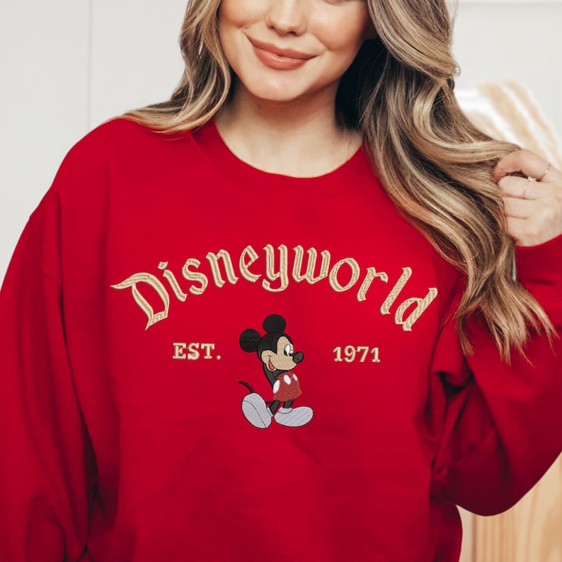 A woman wearing a red sweater with the text "Disneyworld EST. 1971" and a Mickey Mouse graphic.