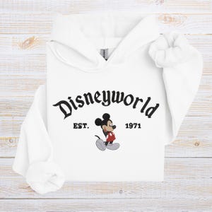 A white hoodie with the text "Disneyworld EST. 1971" and an illustration of Mickey Mouse.