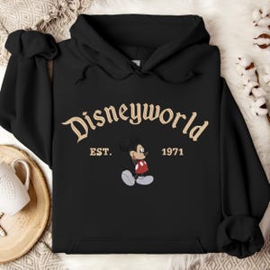 A black hoodie with the text "Disneyworld EST. 1971" and an image of Mickey Mouse, a classic Disney character, printed on it.