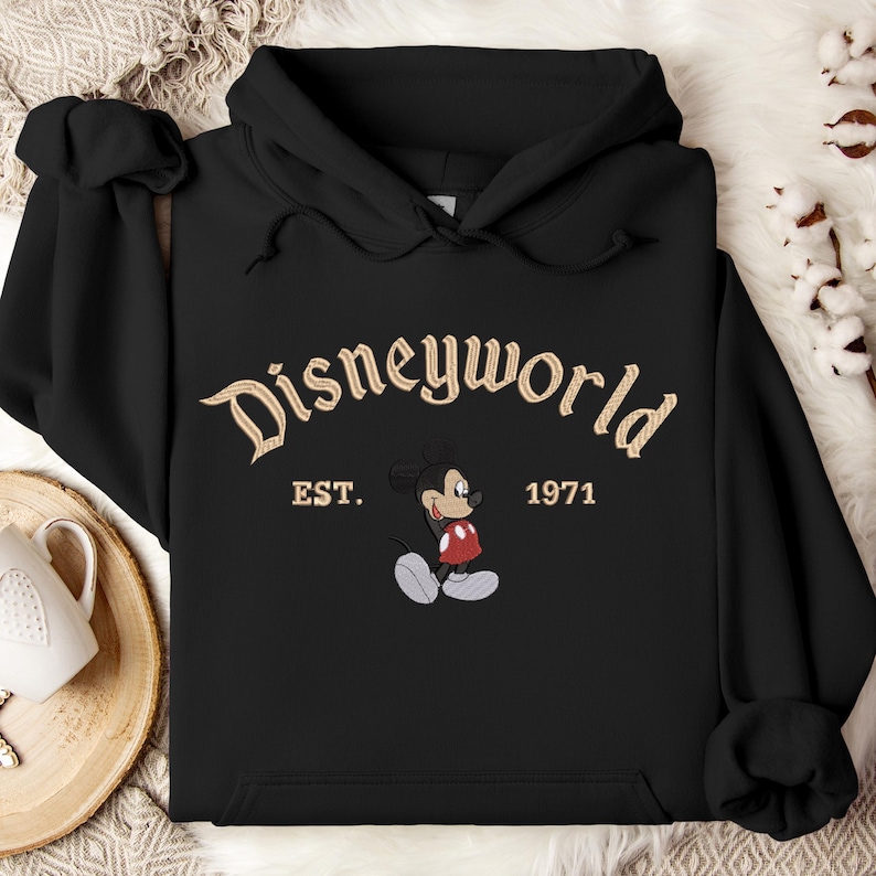 A black hoodie with the text "Disneyworld EST. 1971" and an image of Mickey Mouse, a classic Disney character, printed on it.