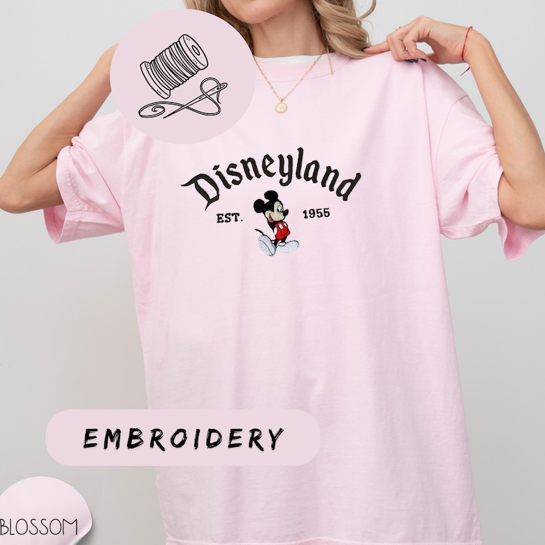 A woman wearing a pink t-shirt with the Disneyland logo and text, posing with her hand on her shoulder.