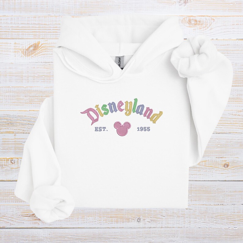 A white hoodie with the text "Disneyland EST. 1955" printed on it, along with a Mickey Mouse logo.