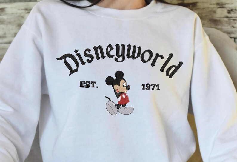 A person wearing a white sweatshirt with the text "Disneyworld EST. 1971" and a Mickey Mouse graphic printed on it.