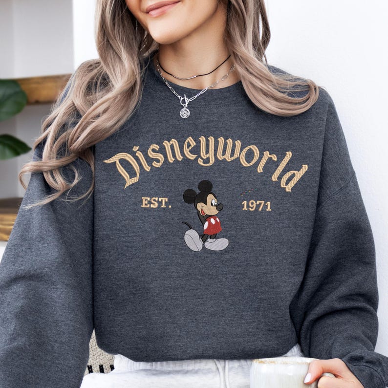A woman wearing a gray sweatshirt with the text "Disneyworld EST. 1971" and a Mickey Mouse graphic printed on it.