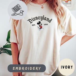 A person wearing a white t-shirt with a Disney Mickey Mouse logo and text, along with a sewing kit icon and the word "Embroidery" below it.