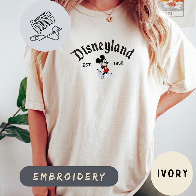A person wearing a white t-shirt with a Disney Mickey Mouse logo and text, along with a sewing kit icon and the word "Embroidery" below it.