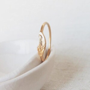 Op de afbeelding: Een gouden ring met een getextureerd, witgouden ontwerp. De ring ligt op een wit keramiek schaaltje.