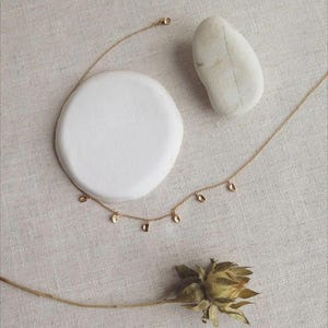 Peut inclure: Un collier à chaîne doré délicat orné de plusieurs petites breloques en forme de goutte d'eau régulièrement espacées. Le collier est disposé en une courbe douce, mettant en valeur les fins maillons métalliques et la finition polie.