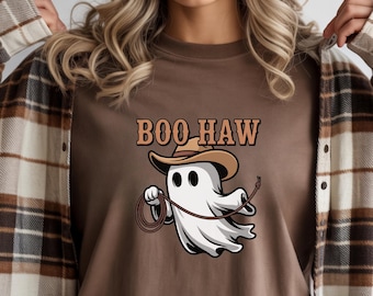 May include: Brown t-shirt with the text "BOO HAW" above a cartoon ghost wearing a cowboy hat and holding a lasso. The ghost is white with black eyes. The shirt is worn with a brown and tan plaid flannel.