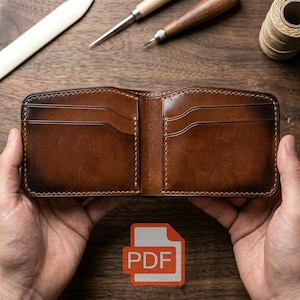 Può includere: Portafoglio in pelle marrone aperto con più fessure per carte, tenuto aperto. Il portafoglio ha un bordo cucito e una finitura lucida. Lo sfondo include strumenti per la lavorazione della pelle e una bobina di filo. Un'icona PDF si trova nell'angolo in basso a destra.