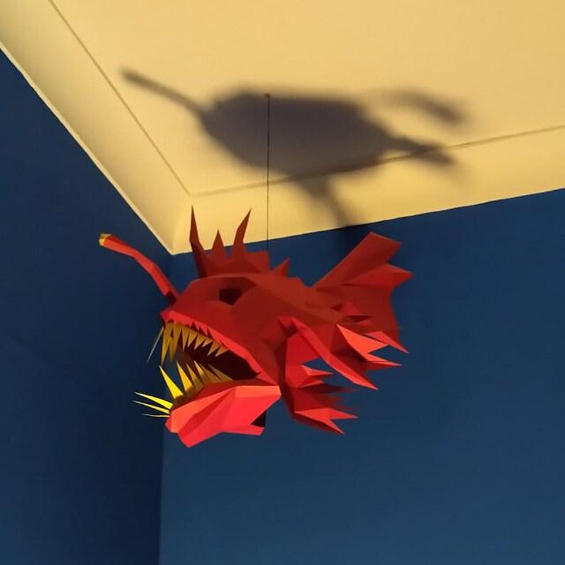 May include: A red paper mache anglerfish sculpture hanging from the ceiling. The fish has a large mouth with sharp teeth and a long, thin lure.