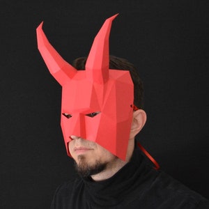 以下が含まれることがあります： 悪魔やデーモンを思わせる、角のある赤い紙製のマスク。マスクはあごひげを生やした人が着用しており、目と鼻を覆っています。