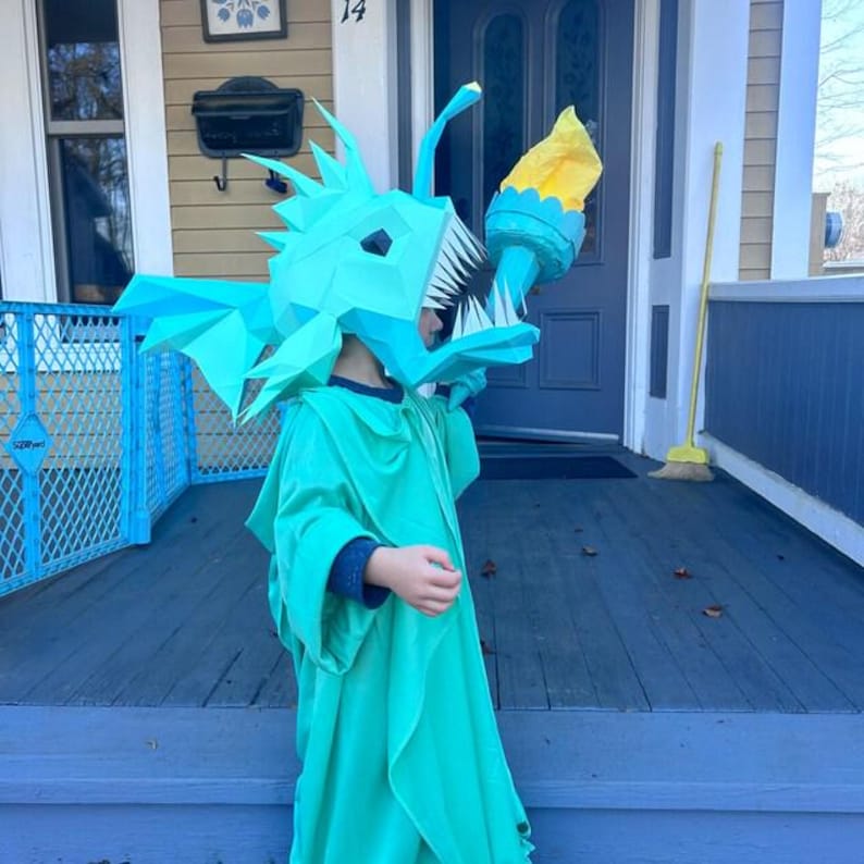 May include: A child dressed as the Statue of Liberty wearing a blue anglerfish costume with a yellow torch.