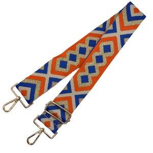 May include: An orange and blue patterned bag strap with gold-colored hardware. The strap features a geometric design with blue diamond shapes and gold accents. The strap is designed to be attached to a bag.