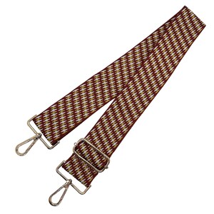 May include: A burgundy and gold patterned bag strap with silver-tone metal hardware. The strap features a repeating geometric design in burgundy, gold, and white. The strap has two silver-tone metal swivel clasps and a silver-tone metal adjustable buckle.
