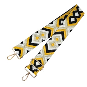 May include: A black, yellow, and white patterned woven strap with gold metal clasps. The strap is designed for a bag or purse.