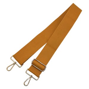 May include: Mustard-colored canvas bag strap with silver-tone metal hardware. The adjustable strap features two swivel snap hooks for easy attachment and a rectangular buckle for adjusting the length. The strap is made of a durable, woven material.