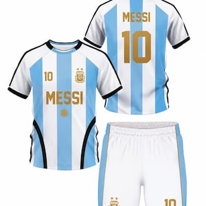 Puede incluir: Un conjunto de camiseta de manga corta y pantal&oacute;n corto con las rayas verticales azul claro y blancas de la selecci&oacute;n nacional de Argentina. La camiseta muestra el nombre MESSI y el n&uacute;mero 10 en dorado, junto al escudo AFA y un sol.