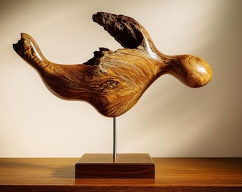 May include: A unique wooden sculpture with a flowing, organic form. The sculpture is made of polished wood, showcasing the natural grain and texture. It is mounted on a square wooden base with a metal rod.