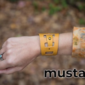 May include: A mustard yellow leather bracelet with a cut-out design and a brass button.