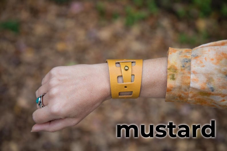 May include: A mustard yellow leather bracelet with a cut-out design and a brass button.