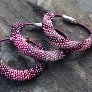 May include: Three beaded bracelets in shades of pink and purple with a silver clasp. The bracelets are made of small beads and are arranged in a spiral pattern.